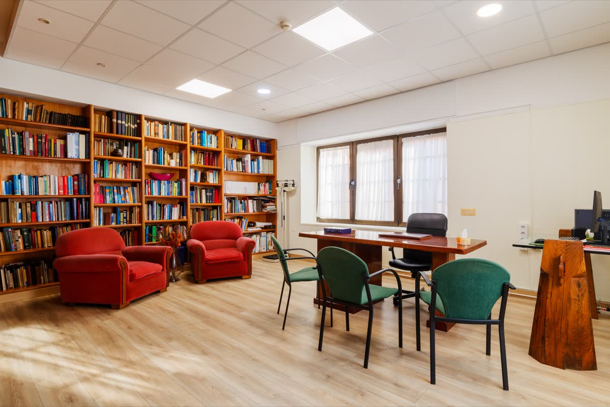 Despacho de consulta con mesa, butacas y una pared entera de estanterías de libros